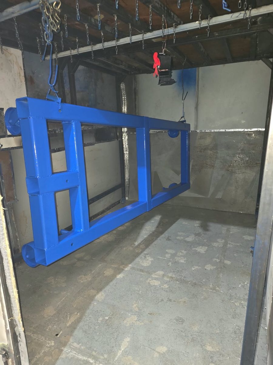 Bastidor de acero rectangular pintado de azul brillante, colgado dentro de la cabina de pintura