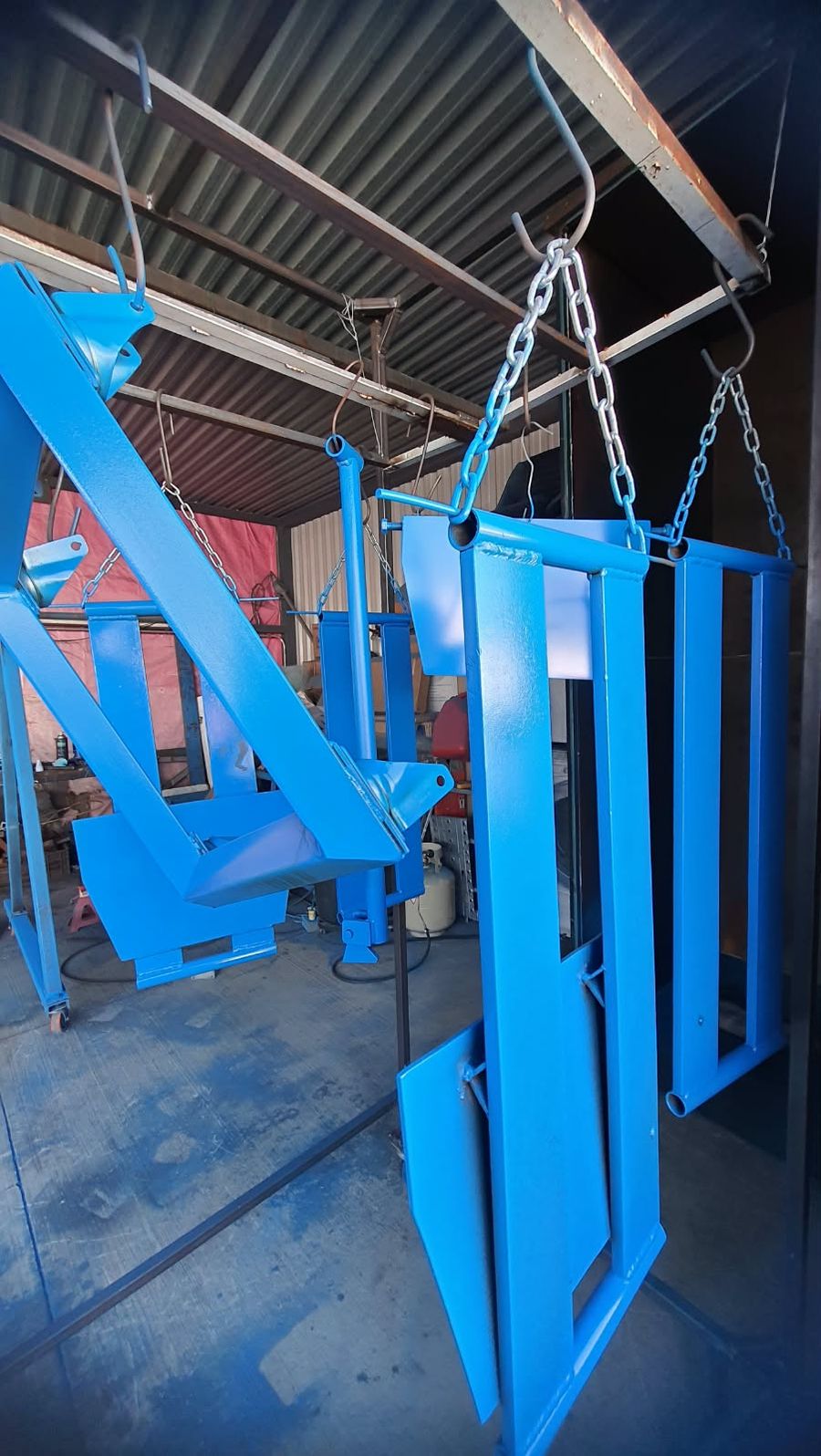 Piezas de acero con acabado azul colgadas de cadenas y ganchos dentro de la cabina